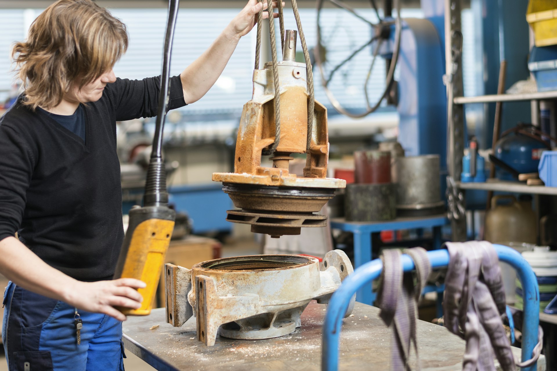 Mitarbeiterin prüft ein am Kran hängendes Pumpenteil in der Werkstatt.
