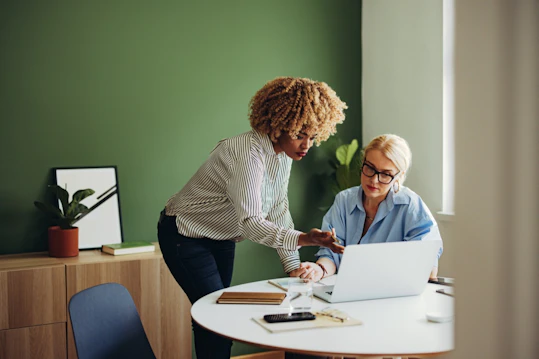 Two colleagues review work on a laptop during a one‑on‑one meeting.