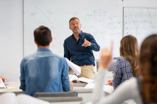 Instructor leads a classroom discussion in front of a whiteboard with diagrams.