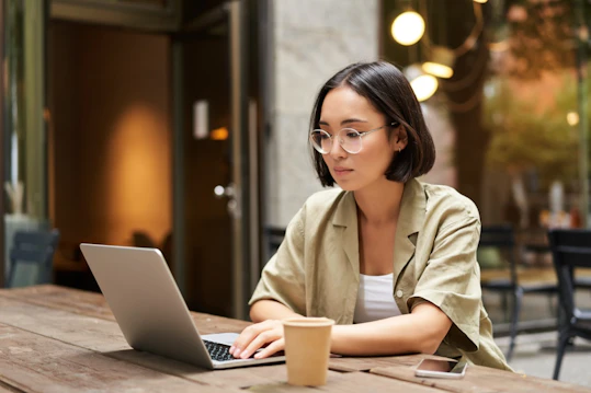 Working outdoors with laptop Person types on a laptop at an outdoor café table with a coffee cup nearby