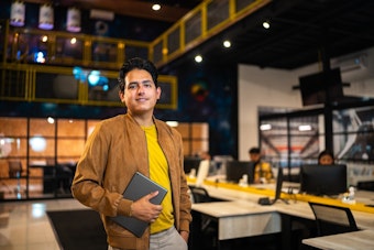 Professional holds a tablet while standing in a bright, modern startup workspace.