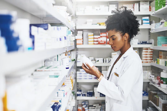 A female pharmacist wearing a white lab coat inspects a medicine bottle.