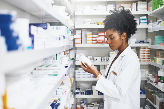A female pharmacist wearing a white lab coat inspects a medicine bottle.