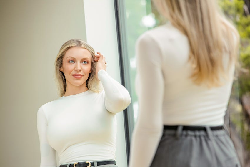 woman looking in mirror touching hair
