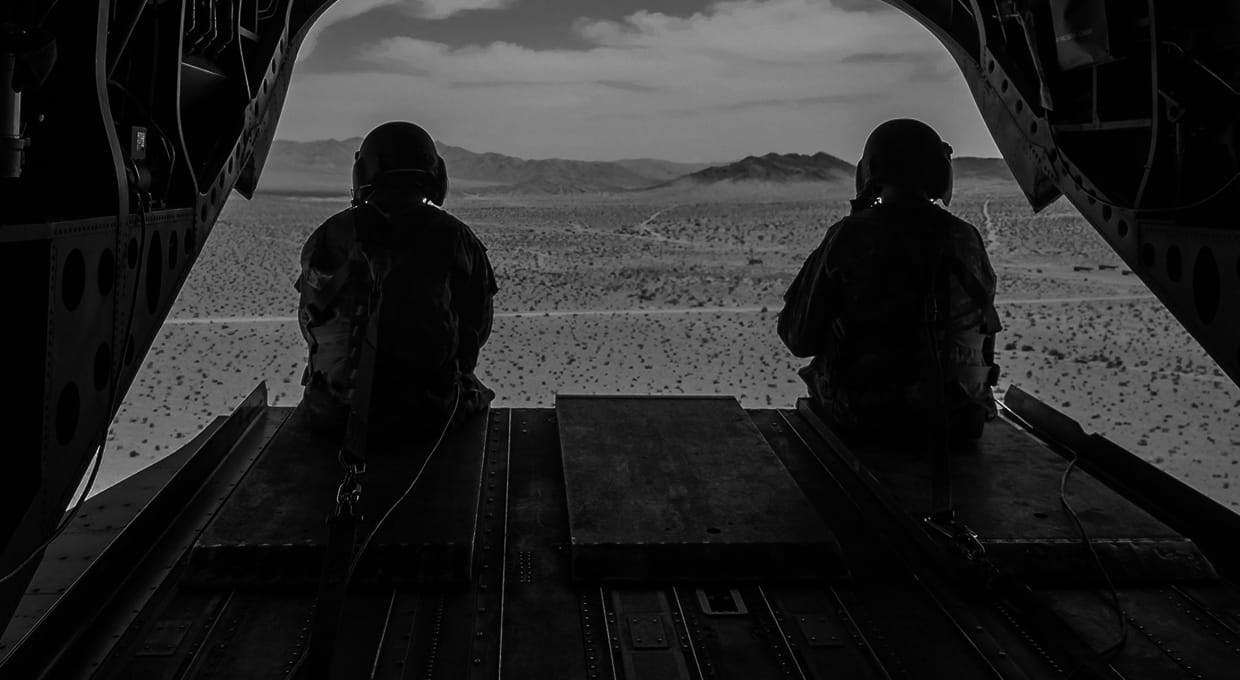 Two soldiers looking out of the back of an airplane