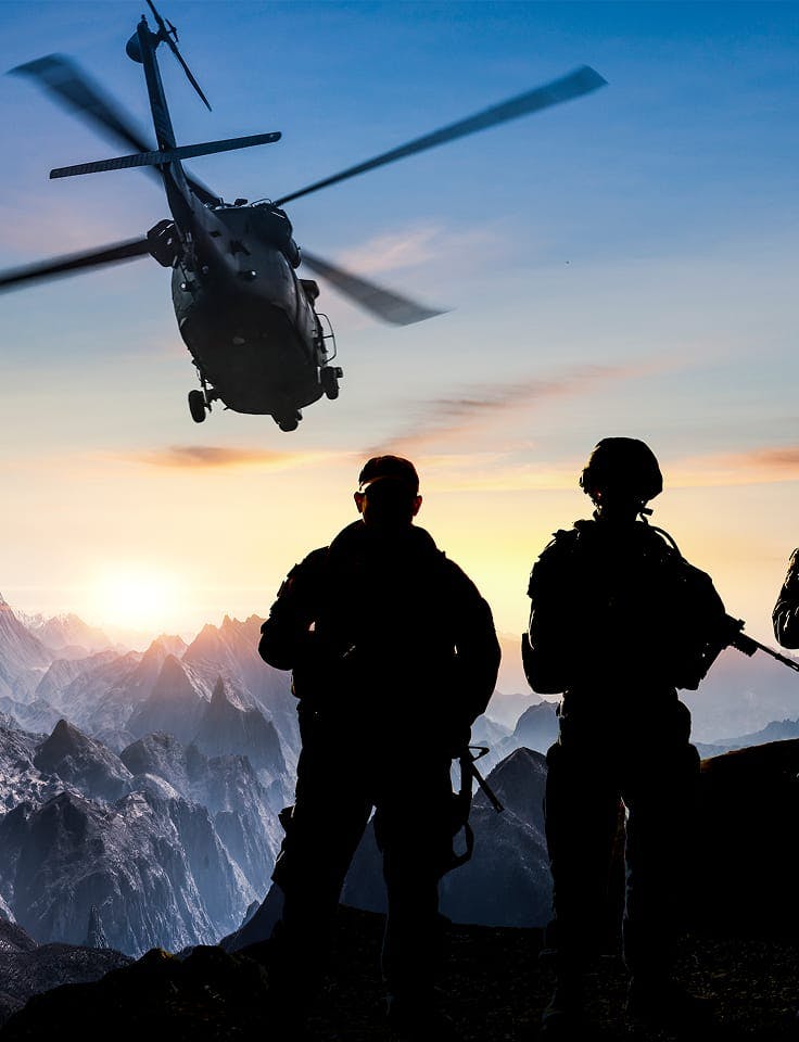 Soldiers silhouetted beneath helicopter at sunset