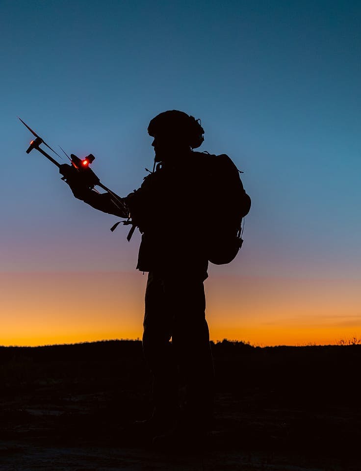 army man holding a drone at dusk
