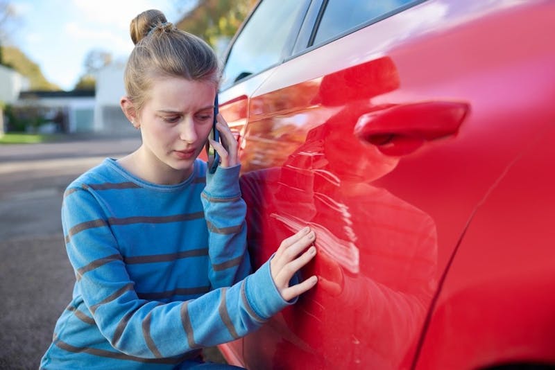 woman checking out the damage on her red car