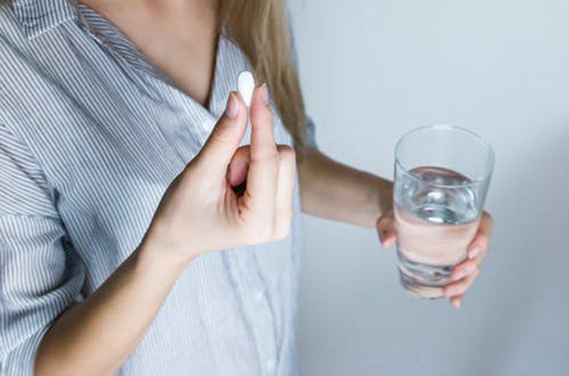 woman taking a pill holding a glass of water