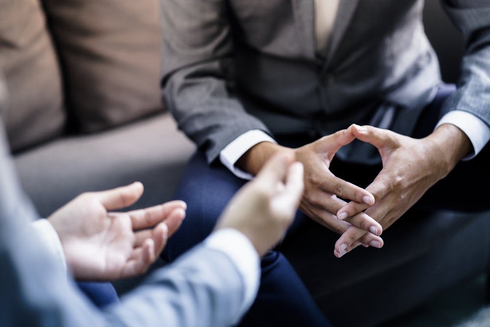 Man with hands clasped talking to another