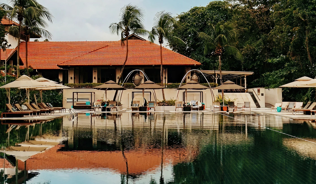 Wide shot of a green pool surrounded by tropical greenery and an asian style building