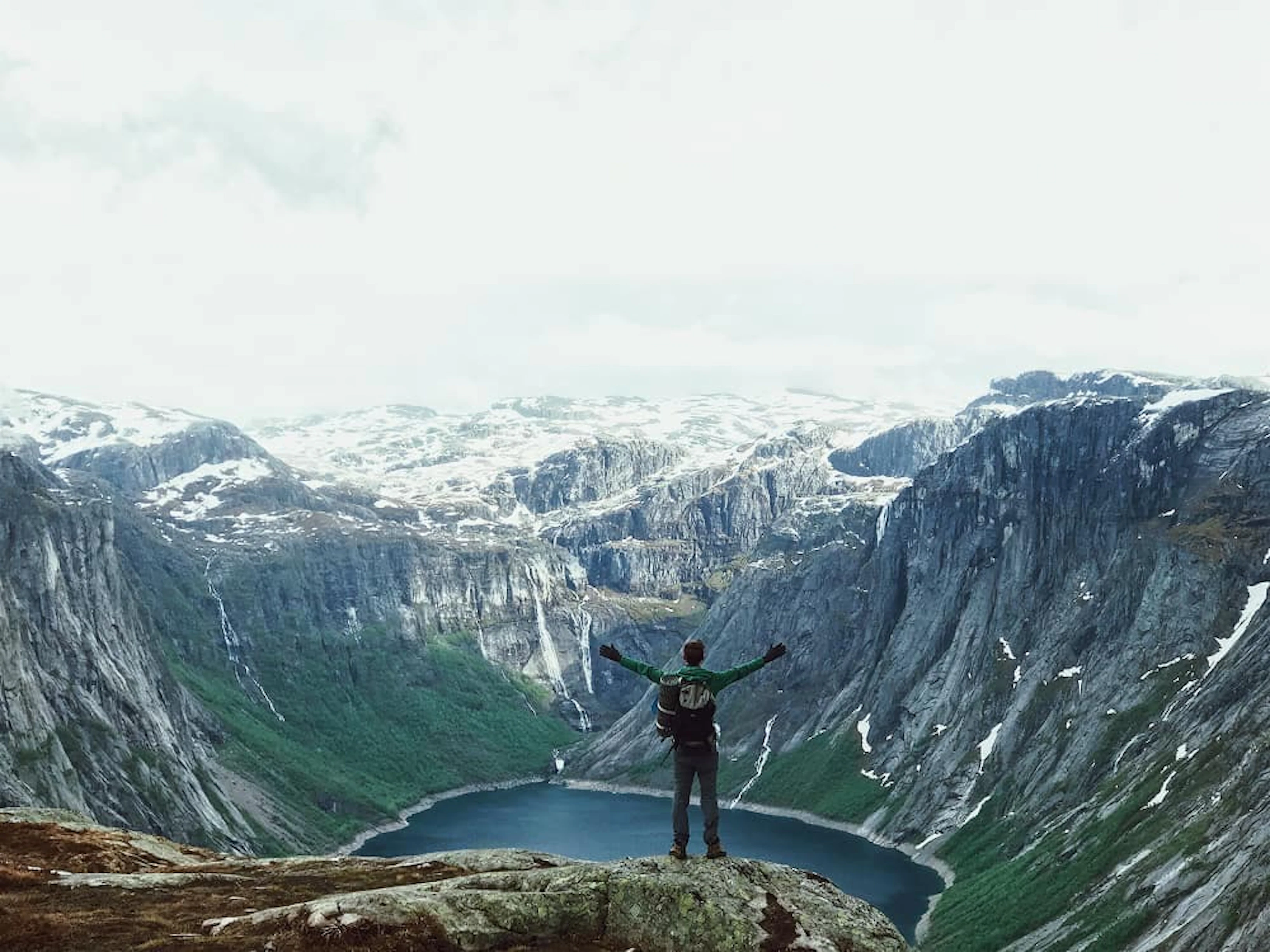 homme qui écarte les bras face à un cirque de montagne avec un lac en bas et de la neige sur les pics