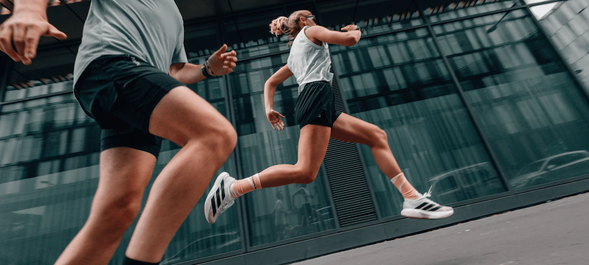 femme et homme en short qui courent devant une façade vitrée