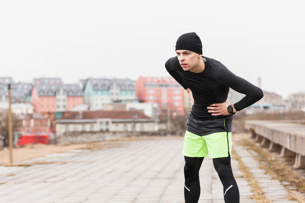 homme en tenue de sport noire et verte se tient les côtes en étant penché en avant