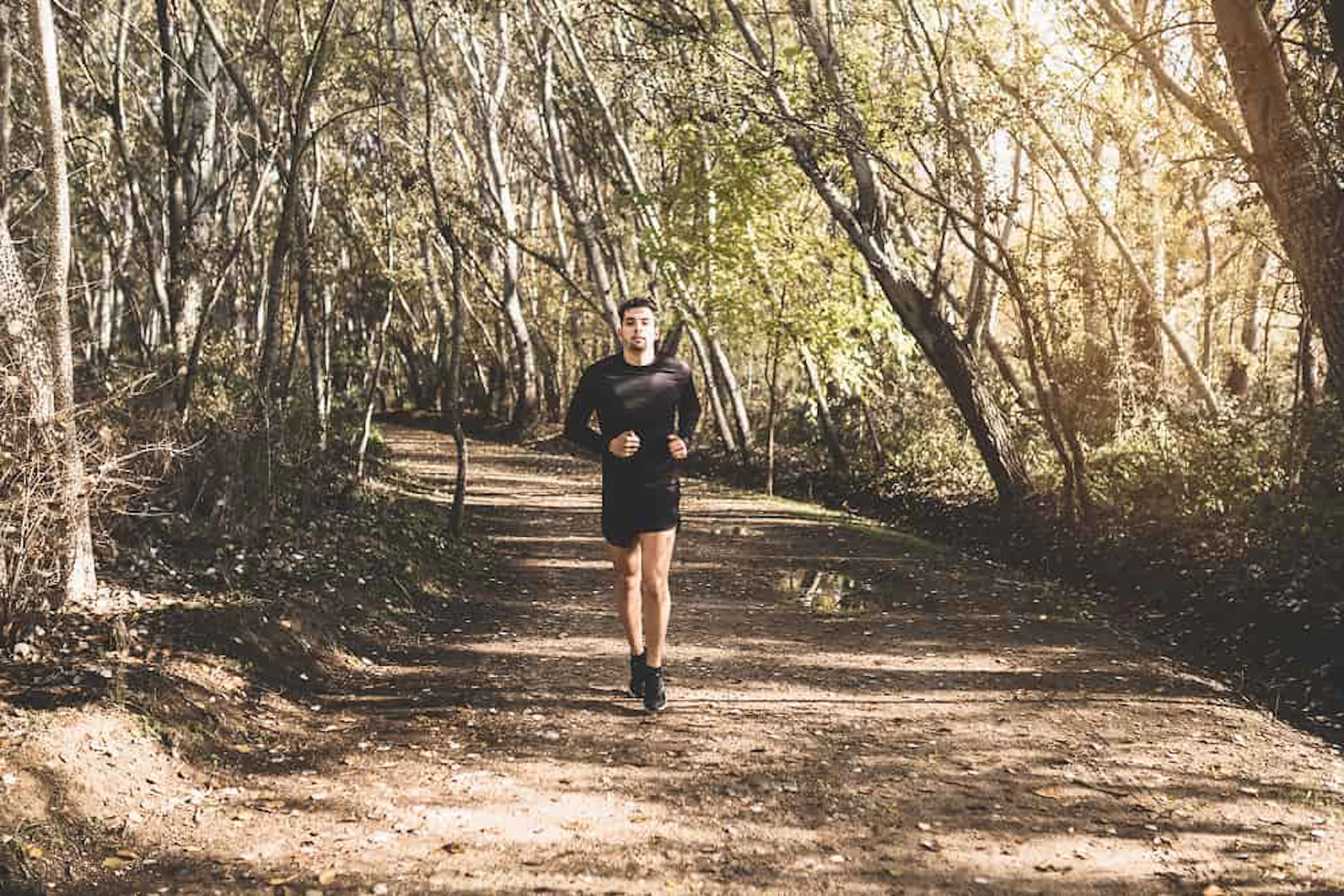 un homme court en noir sur un sentier au milieu d'une forêt (10 km du bois de boulogne)