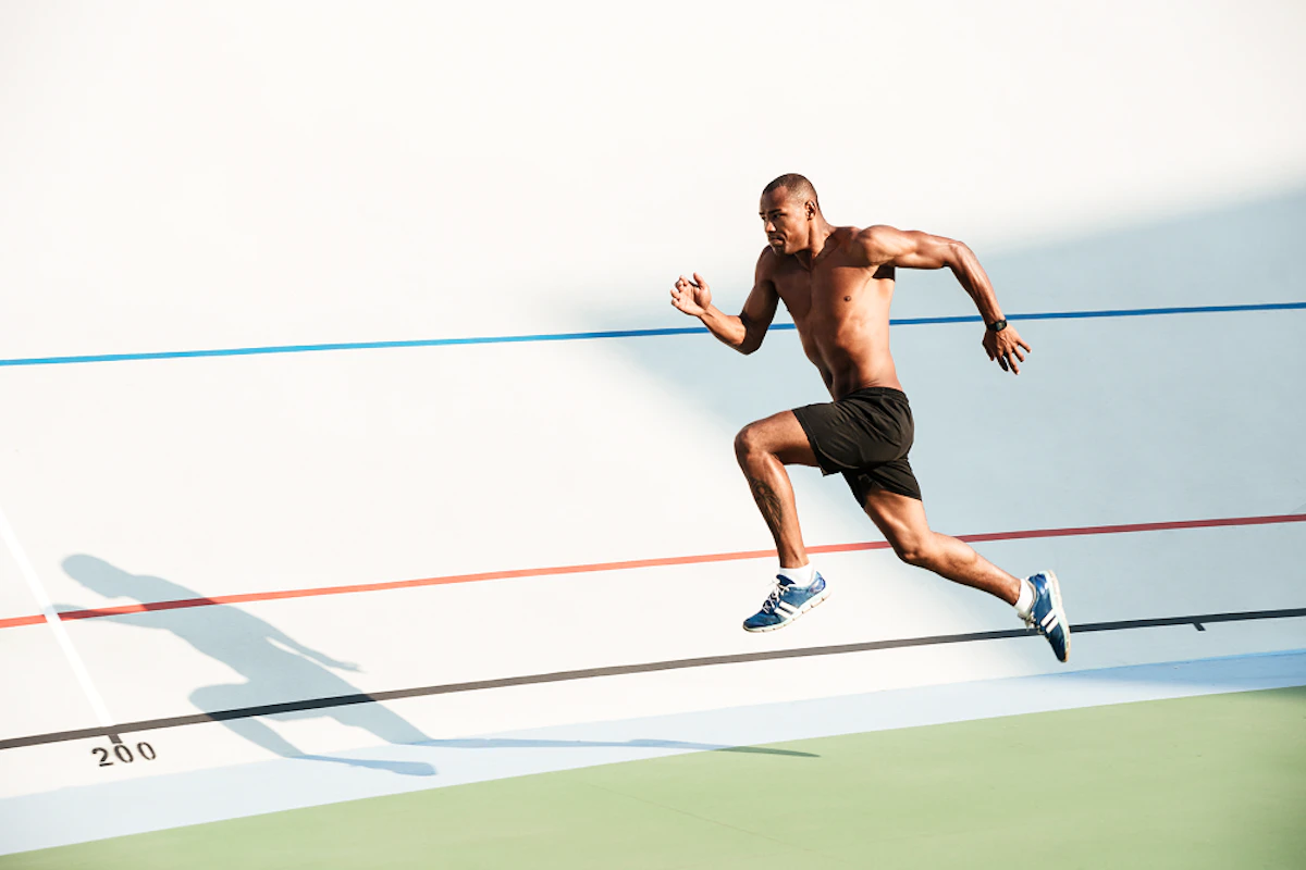 homme torse nu sprinte sur une piste blanche avec des lignes bleues, blanches, rouges