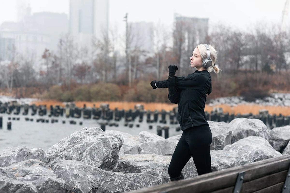 femme blonde habillée en noir avec un casque audio s'étire les bras devant des rochers