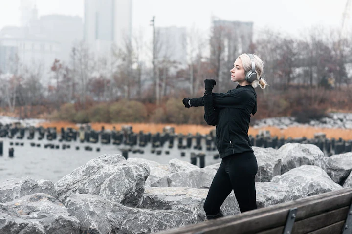 femme blonde habillée en noir avec un casque audio s'étire les bras devant des rochers