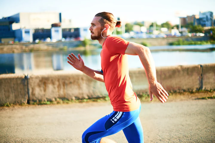 homme avec un tee-shirt orange et un legging bleu court vite avec des écouteurs