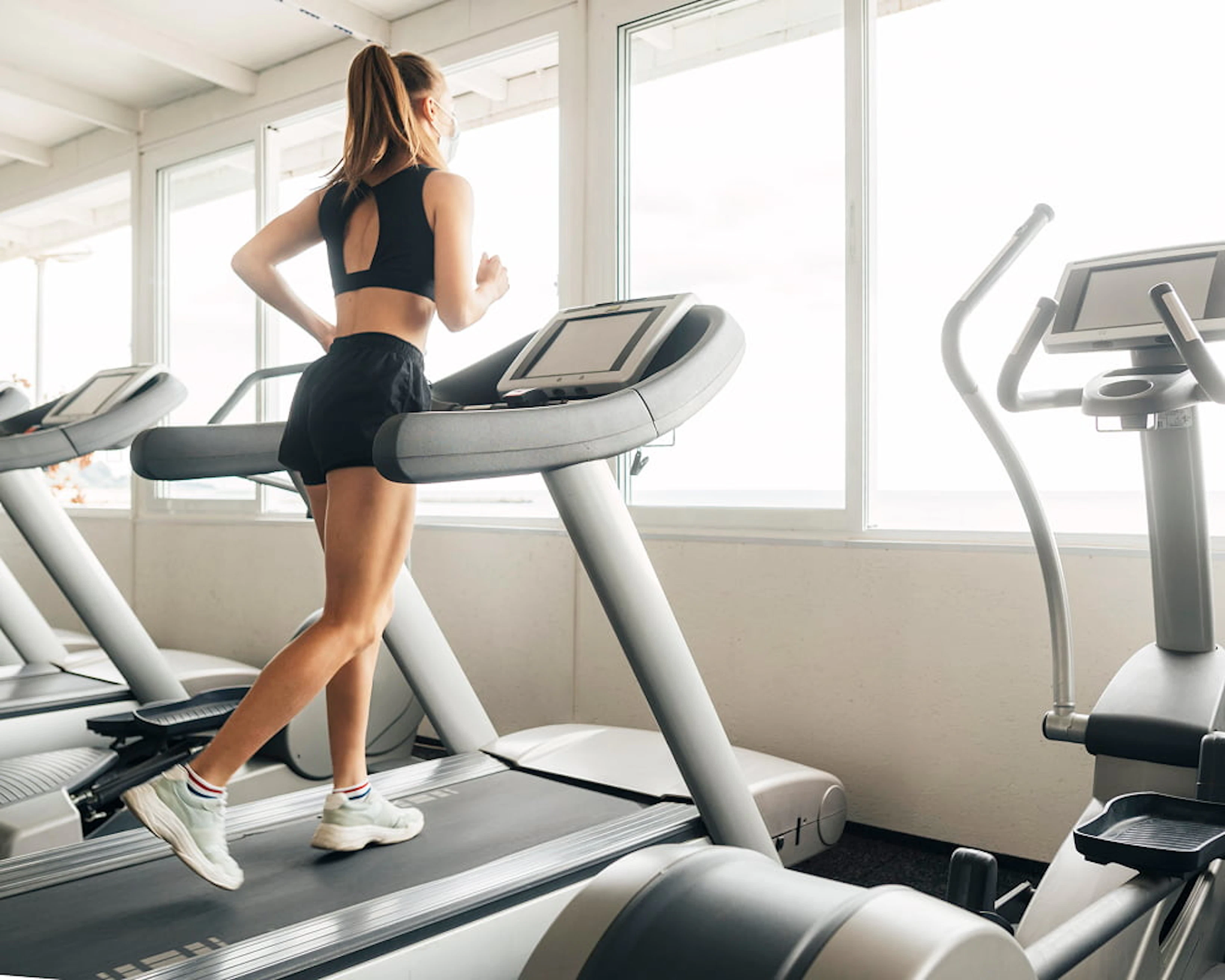 femme habillée en noir court sur un tapis de course face à une fenêtre