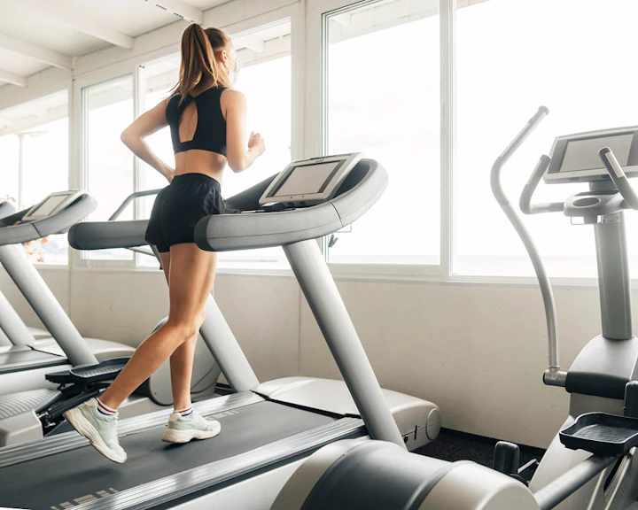 femme habillée en noir court sur un tapis de course face à une fenêtre