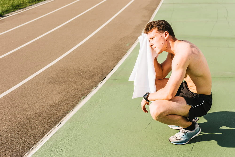 homme torse nu s'essuie le front avec une serviette au bord d'une piste d'athlétisme