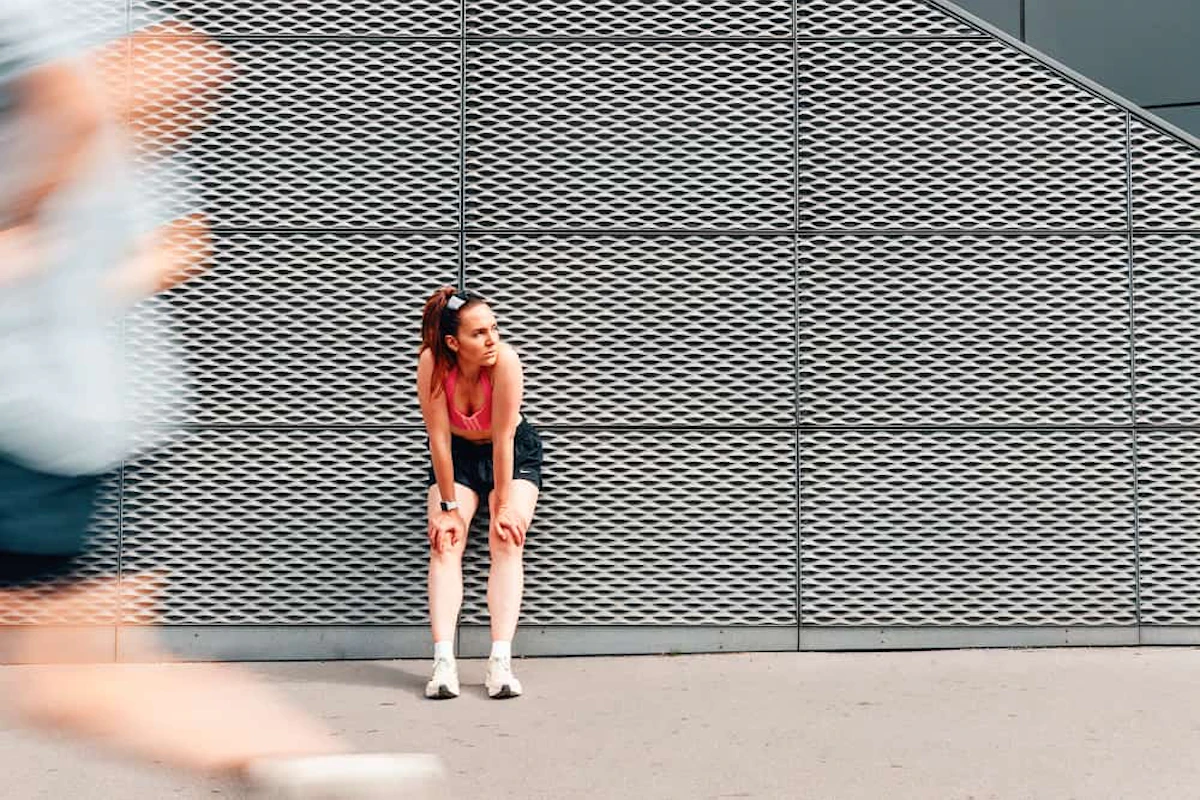 femme adossée à un mur gris et coureur flou qui passe devant