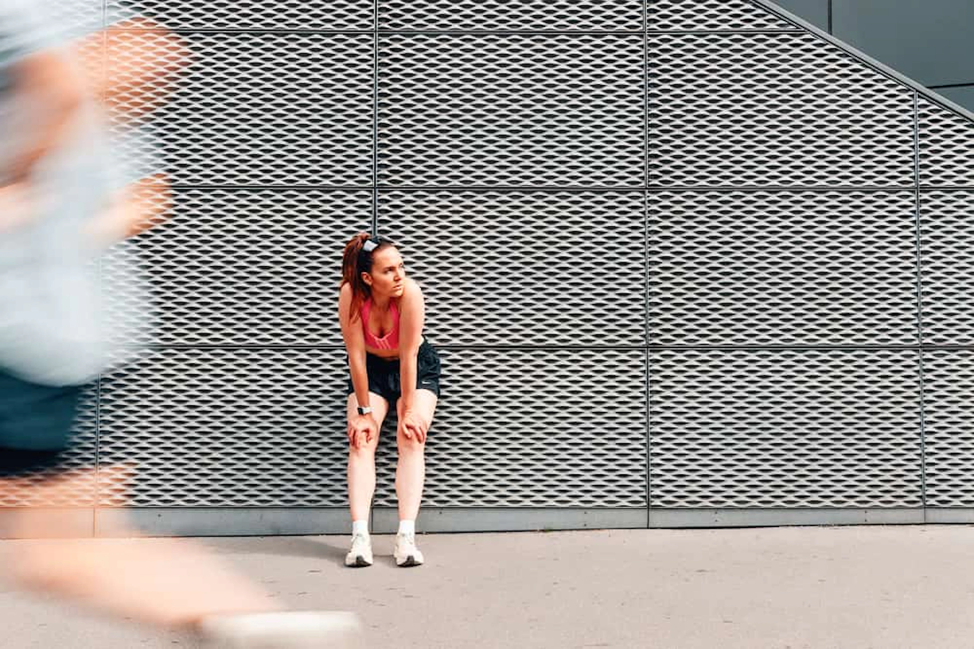 femme adossée à un mur gris et coureur flou qui passe devant