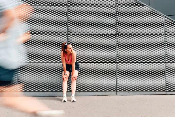 femme adossée à un mur gris et coureur flou qui passe devant