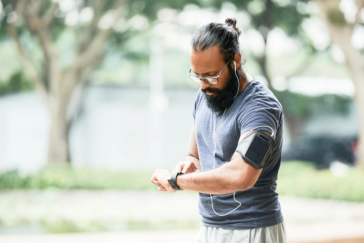 Un homme porte des écouteurs et un brassard, et regarde sa montre connectée