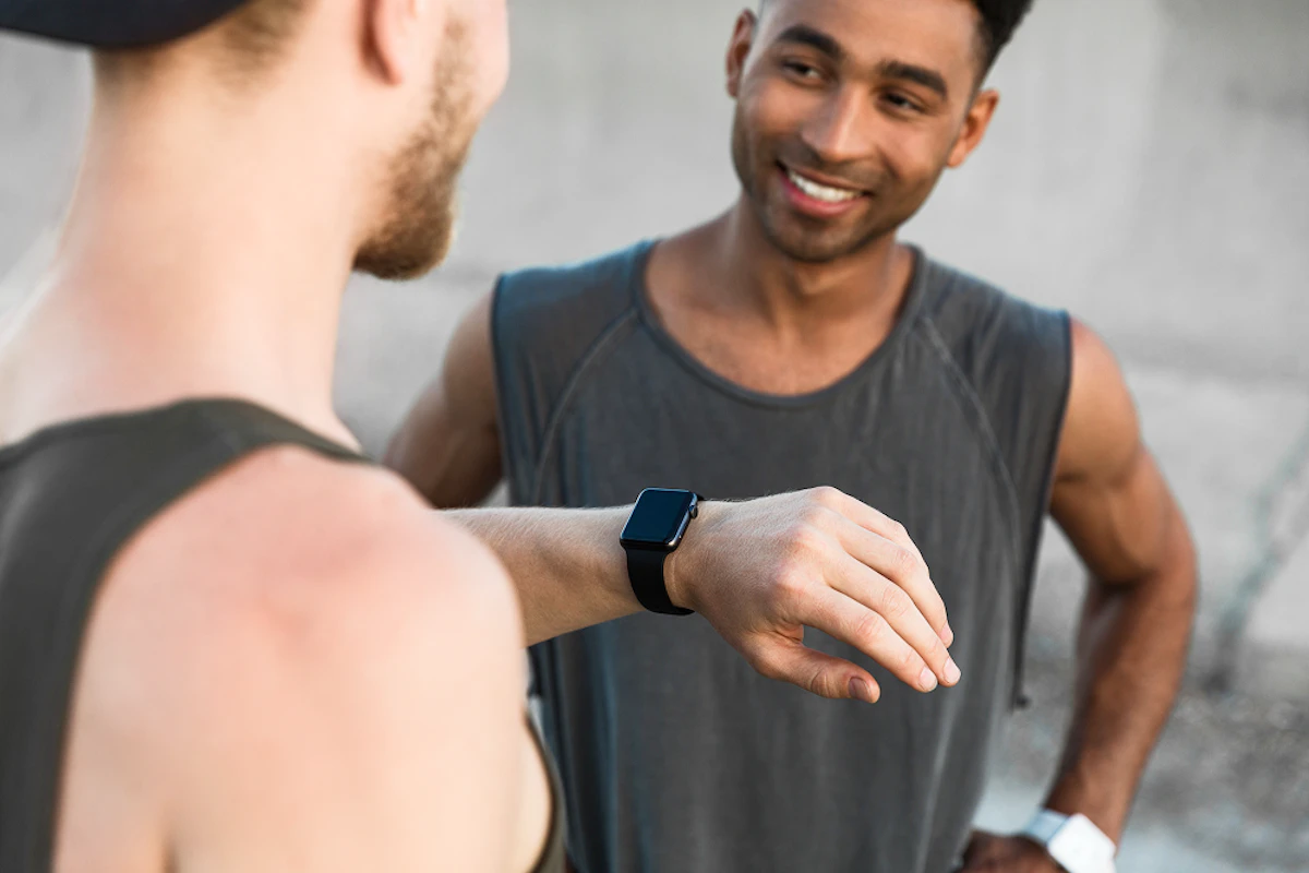 Deux hommes en tenue de course à pied discutent, l'un d'eux regarde sa montre connectée