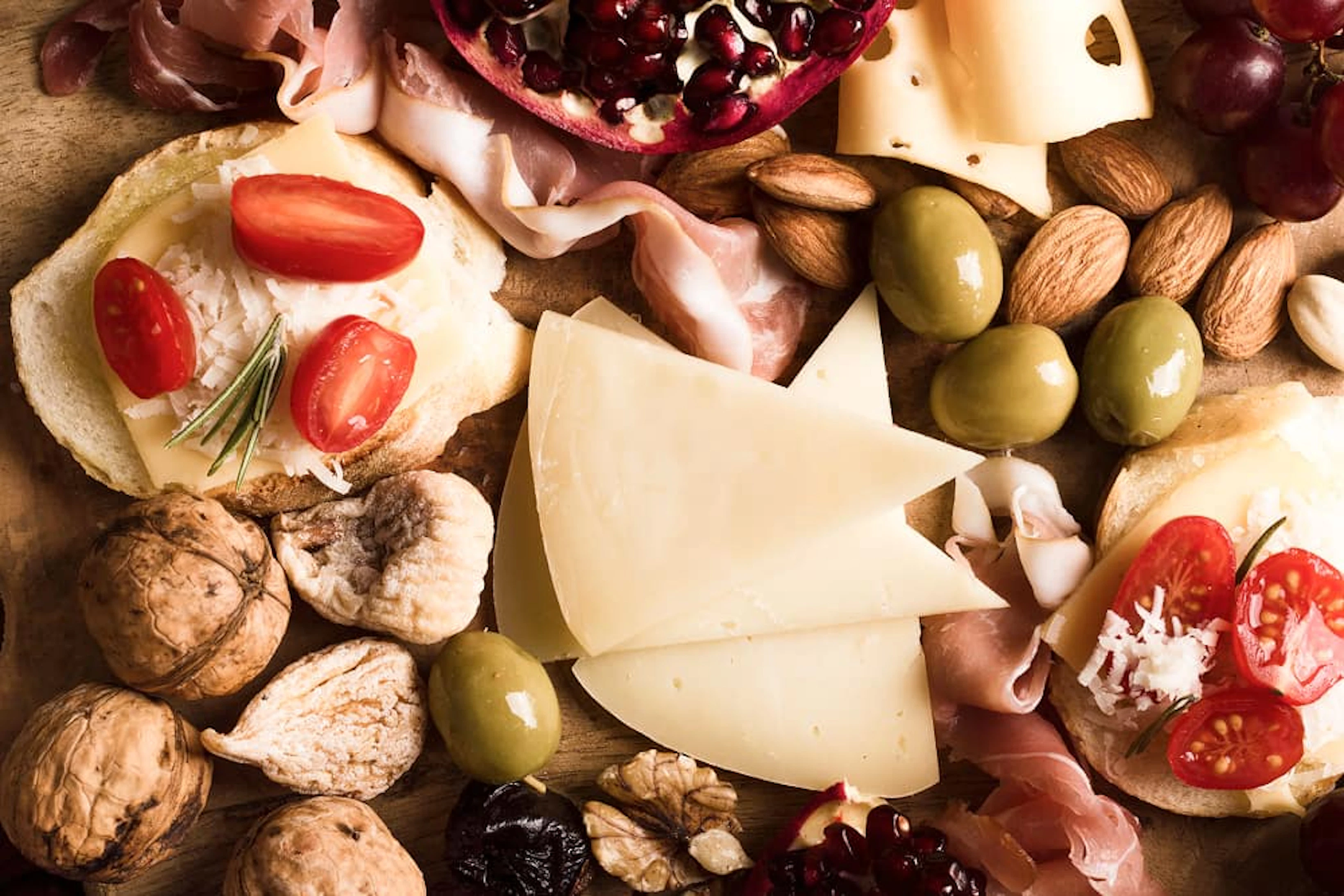 plateau avec du fromage, du jambon cru, des tomates, des noix et des olives