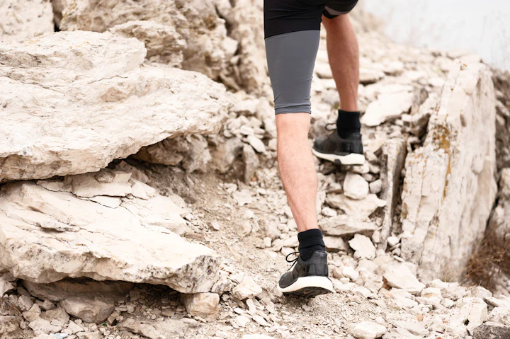 Un homme fait du trail running sur un sentier technique jonché de pierres.