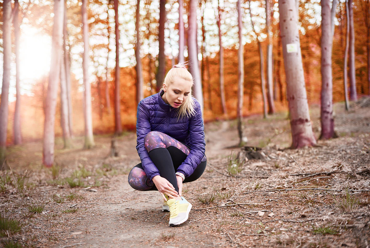 Dans une forêt, une femme en tenue de running se tient la cheville.