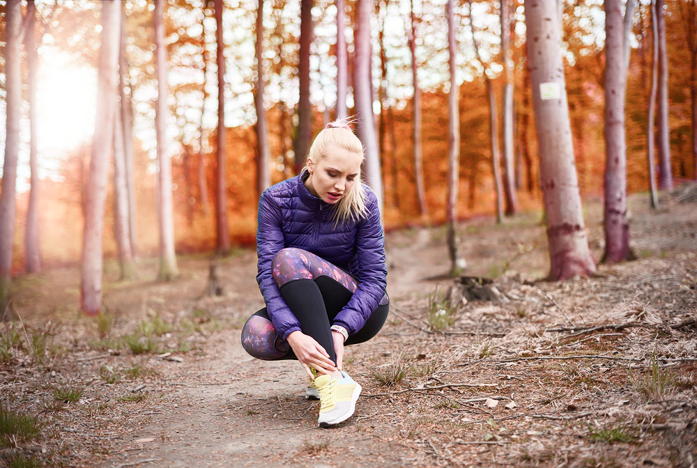 Dans une forêt, une femme en tenue de running se tient la cheville.