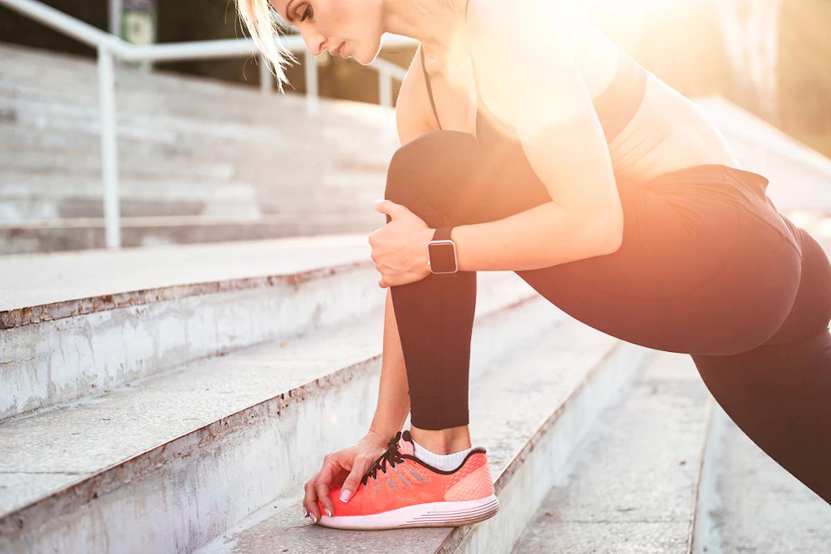 Une femme en tenue de running est en appui sur une marche et se tient la jambe.