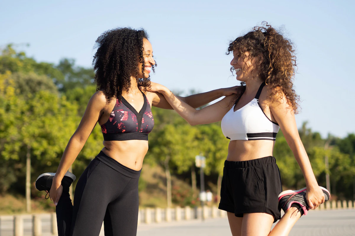 Deux femmes en tenues de running s'étirent et se tiennent par l'épaule en se souriant