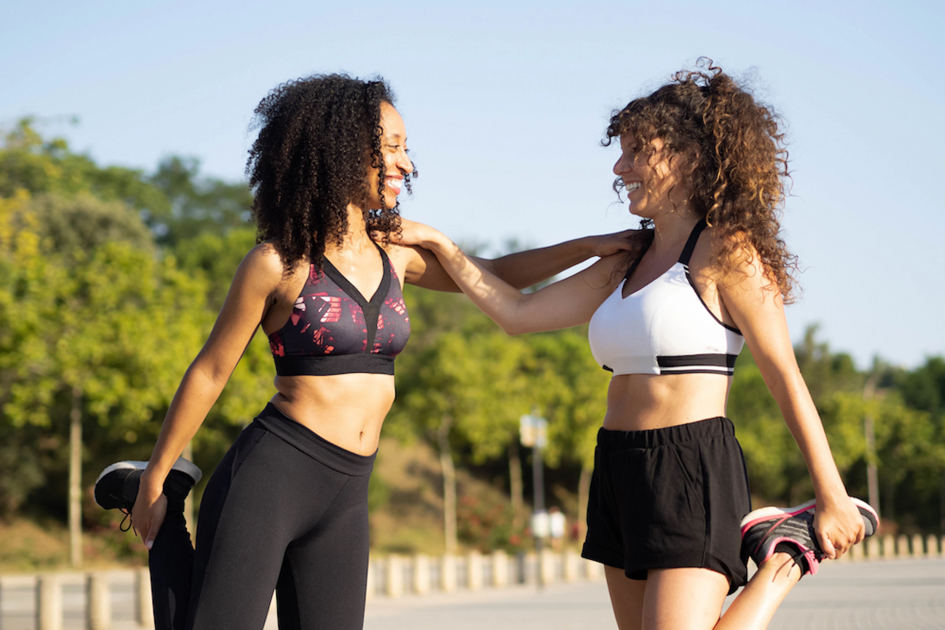 Deux femmes en tenue de running s'étirent et se tiennent par l'épaule en se souriant.