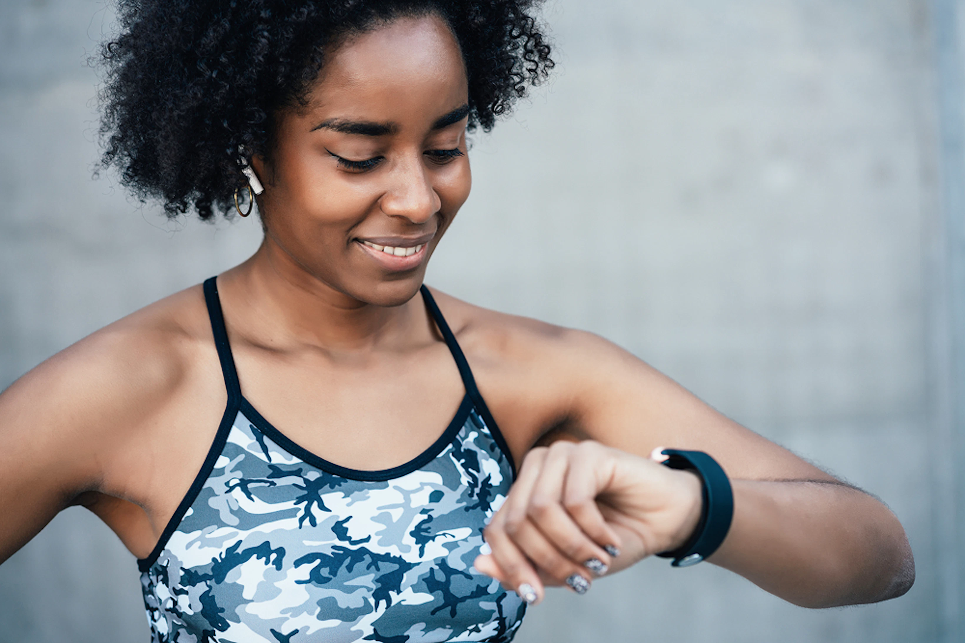 Une femme en tenue de course à pied regarde son chrono en souriant.