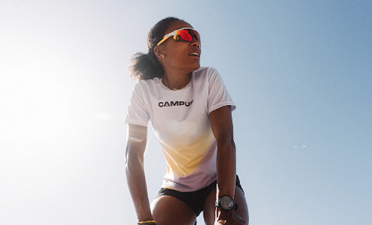 Une femme en tenue de course à pied s'appuie sur ses cuisses et regarde au loin.