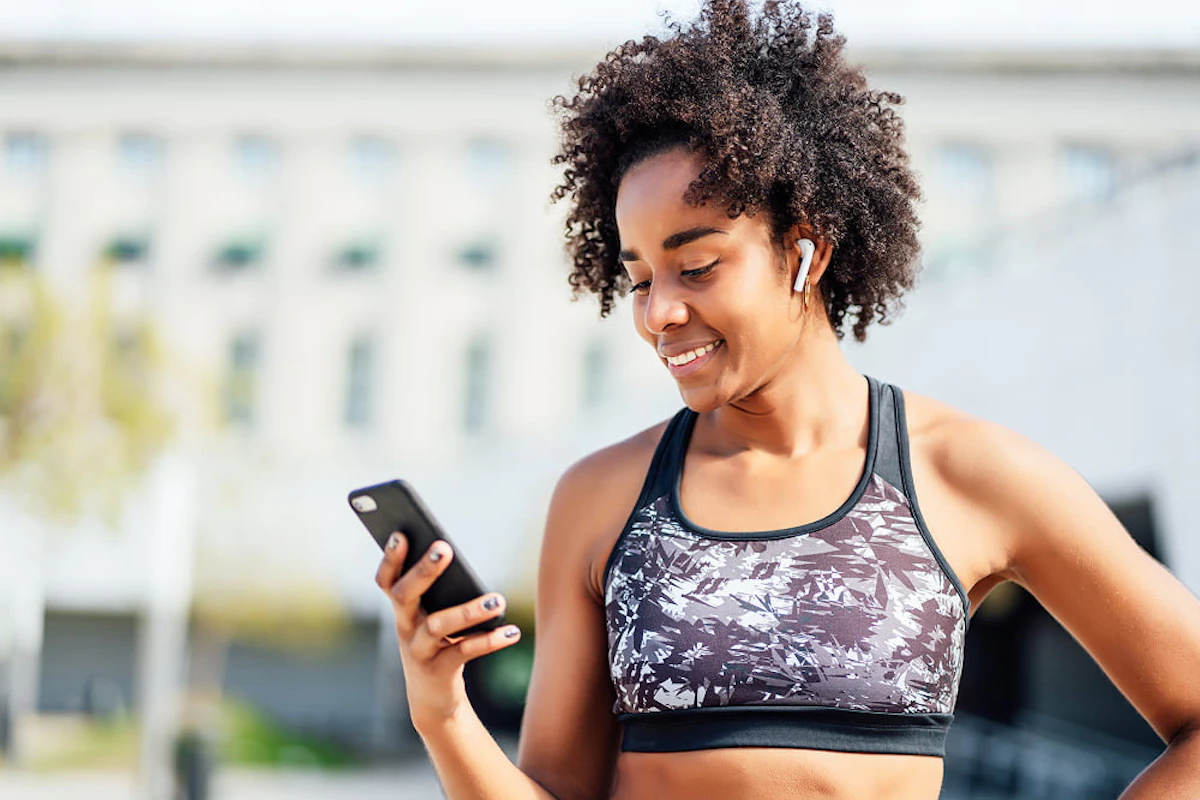 Une femme en brassière regarde son téléphone en souriant.