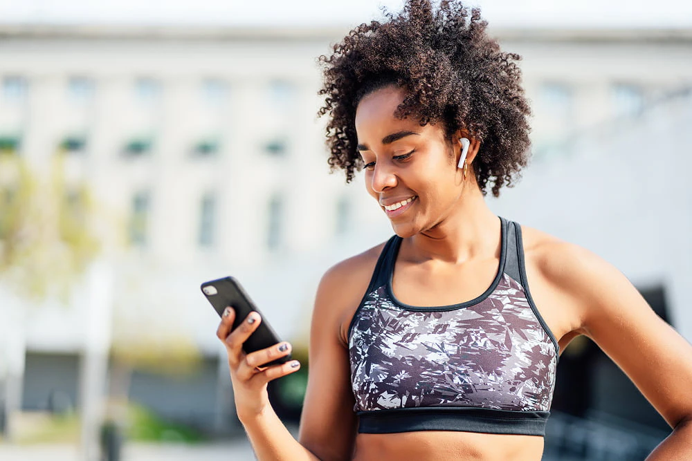 Une femme en brassière regarde son téléphone en souriant.
