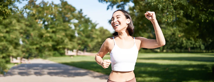 Une femme en tenue de course à pied lève les bras et semble heureuse d'avoir atteint son objectif
