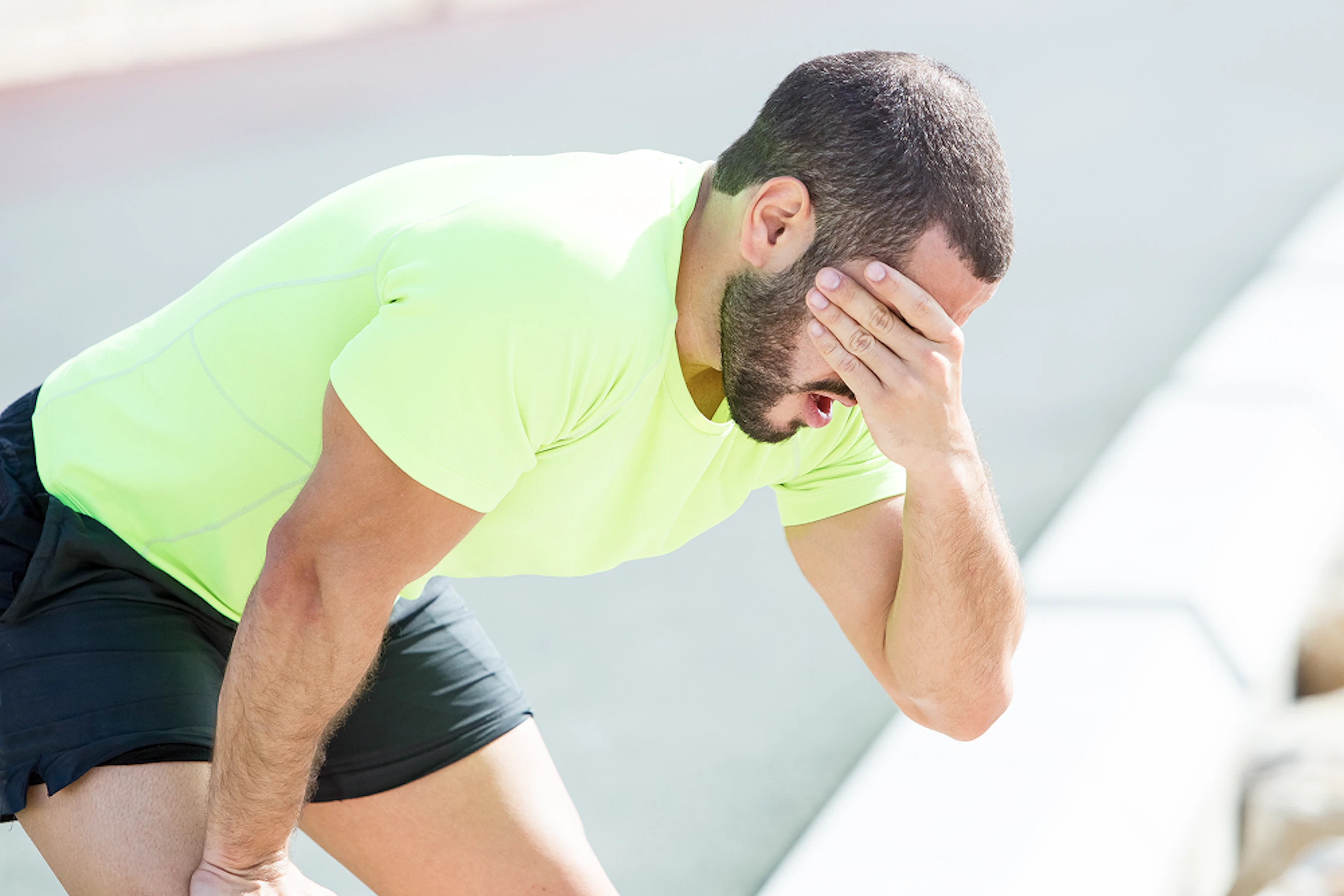 Un homme en tenue de running se tient le visage avec un main et le genou avec l'autre main