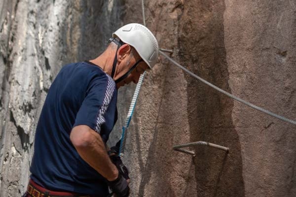 Senior climbing via ferrata in the mountains — activity accessible for adults