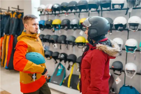Adults trying ski helmets in a sports shop — safety gear for slopes