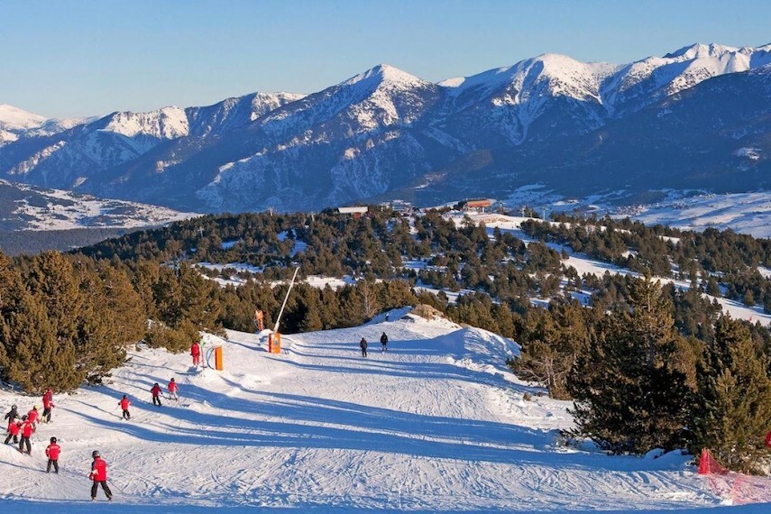 Skieurs sur les pistes boisées de Font-Romeu face aux sommets des Pyrénées