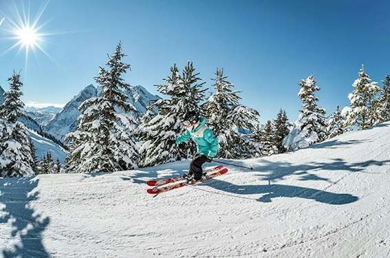 Forfait ski La Clusaz pas cher | Passe Montagne Skieur entre les sapins enneigés de La Clusaz au soleil en Haute-Savoie