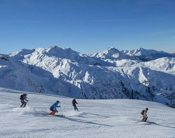 Les Contamines cheap ski pass | Passe Montagne Skiers on a wide run at Les Contamines facing the snowy peaks, Haute-Savoie