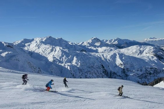 Les Contamines cheap ski pass | Passe Montagne Skiers on a wide run at Les Contamines facing the snowy peaks, Haute-Savoie